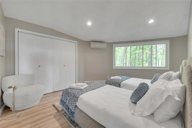 bedroom featuring light hardwood / wood-style floors, an AC wall unit, a closet, and lofted ceiling