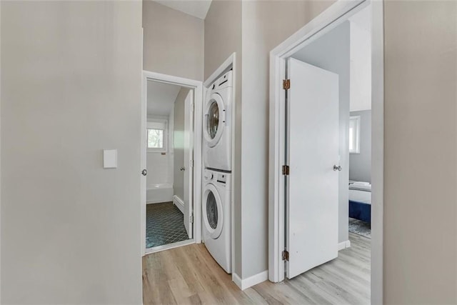 clothes washing area with light hardwood / wood-style flooring and stacked washing maching and dryer