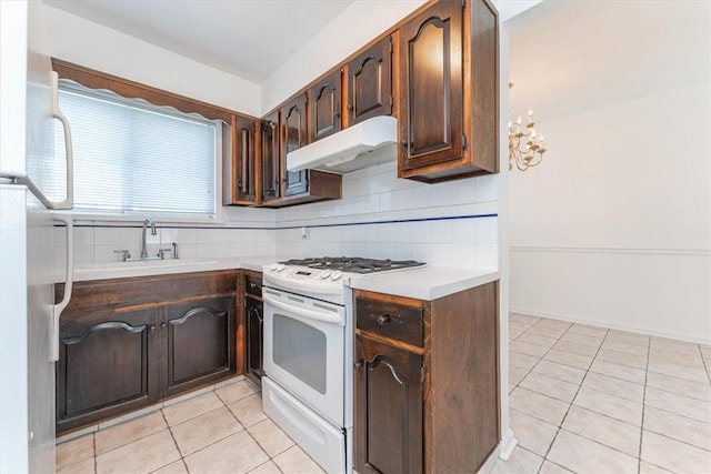 kitchen featuring backsplash, white gas range, dark brown cabinets, light tile patterned floors, and fridge