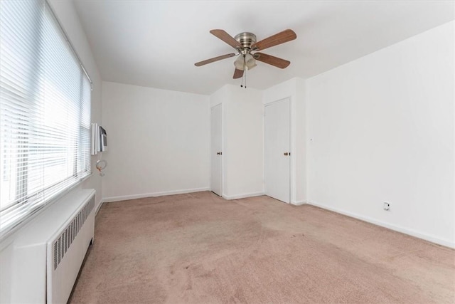 unfurnished room featuring ceiling fan, light colored carpet, and radiator heating unit