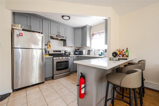 kitchen featuring kitchen peninsula, stainless steel appliances, light tile patterned floors, a breakfast bar, and gray cabinets