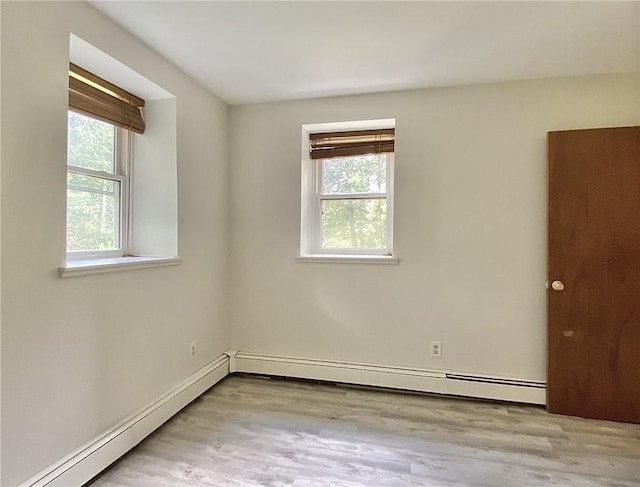 empty room featuring light hardwood / wood-style floors, a wealth of natural light, and a baseboard heating unit