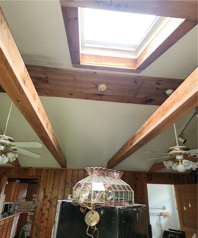details featuring beam ceiling, a skylight, wooden walls, and ceiling fan