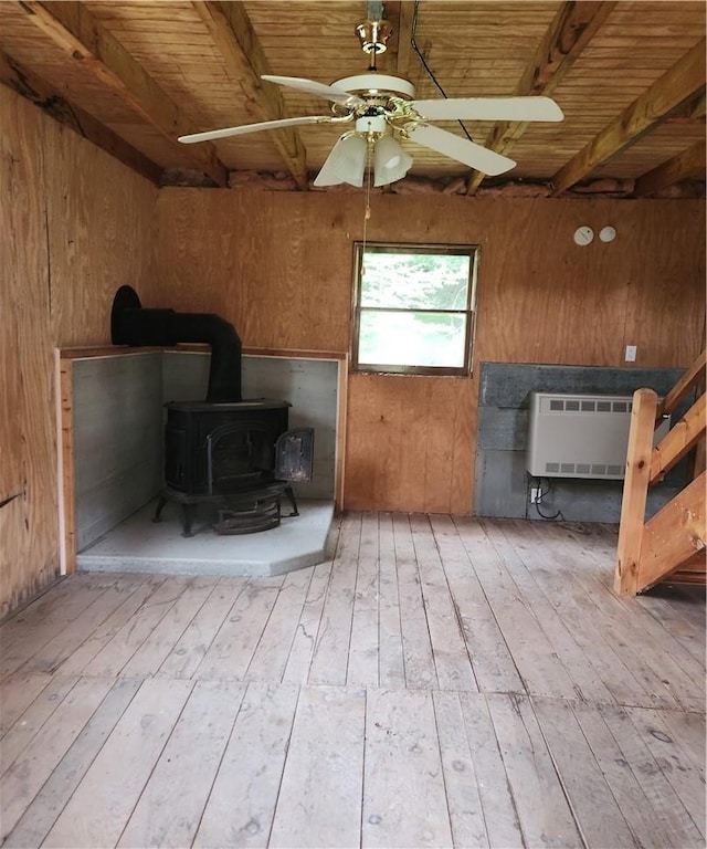 interior space with light wood-type flooring, a wood stove, ceiling fan, and wood walls
