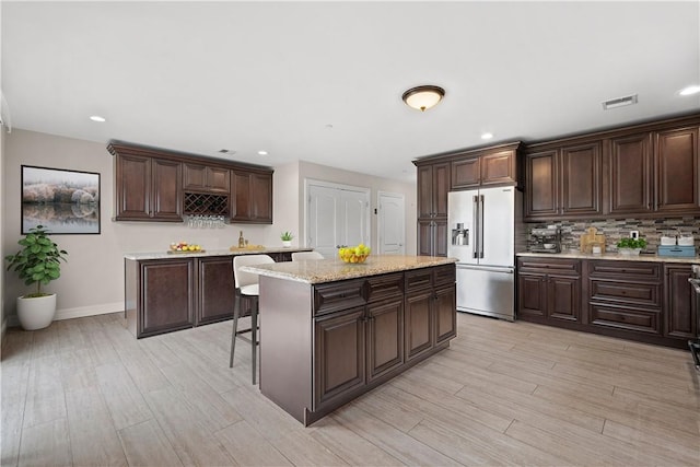 kitchen with light wood-type flooring, high end refrigerator, a center island, and dark brown cabinets