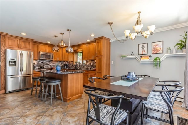 kitchen featuring an inviting chandelier, ornamental molding, appliances with stainless steel finishes, decorative light fixtures, and a kitchen island