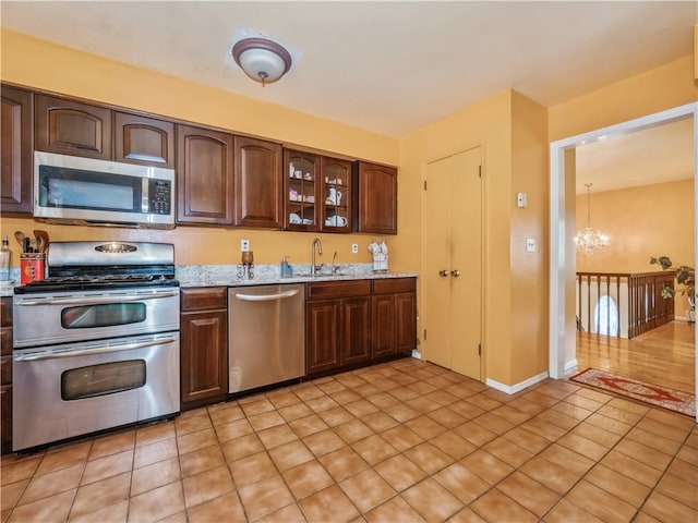 kitchen with sink, light stone counters, dark brown cabinetry, stainless steel appliances, and a chandelier