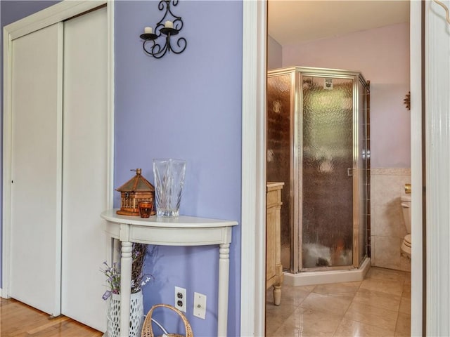 bathroom featuring toilet, tile walls, and a shower with shower door