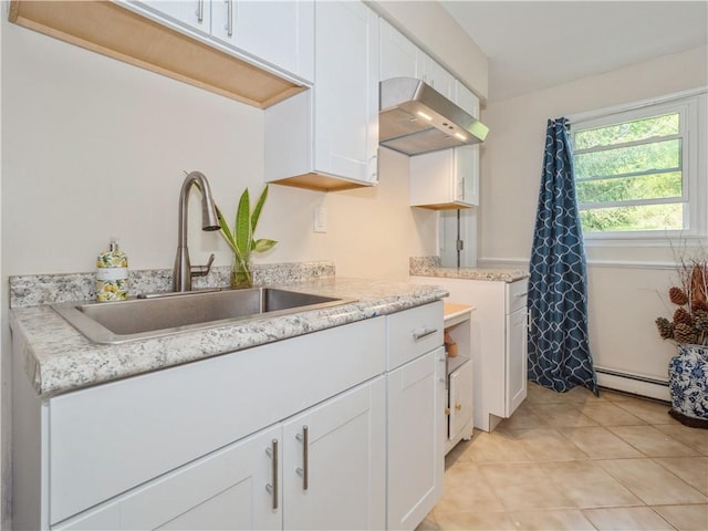 kitchen featuring light stone countertops, baseboard heating, sink, white cabinets, and light tile patterned flooring