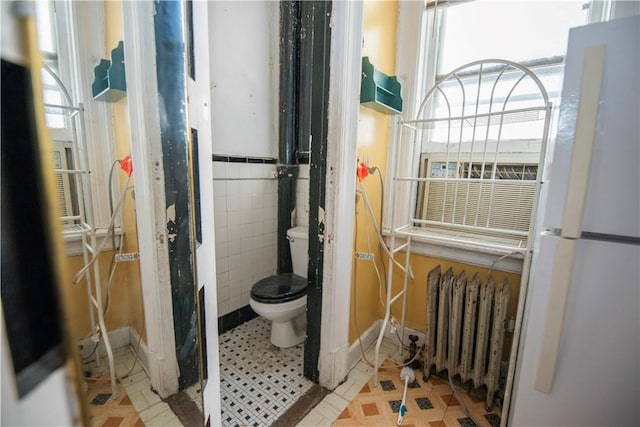 bathroom featuring radiator heating unit, toilet, and tile walls