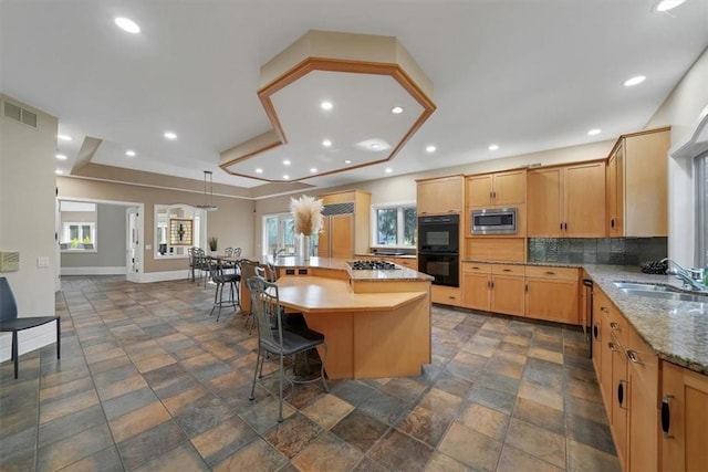 kitchen with stainless steel microwave, sink, tasteful backsplash, a tray ceiling, and a kitchen island