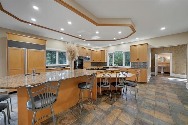 kitchen featuring light stone countertops, light brown cabinetry, a kitchen breakfast bar, a spacious island, and built in appliances