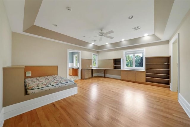 unfurnished bedroom with a tray ceiling, ceiling fan, light hardwood / wood-style flooring, and ensuite bathroom