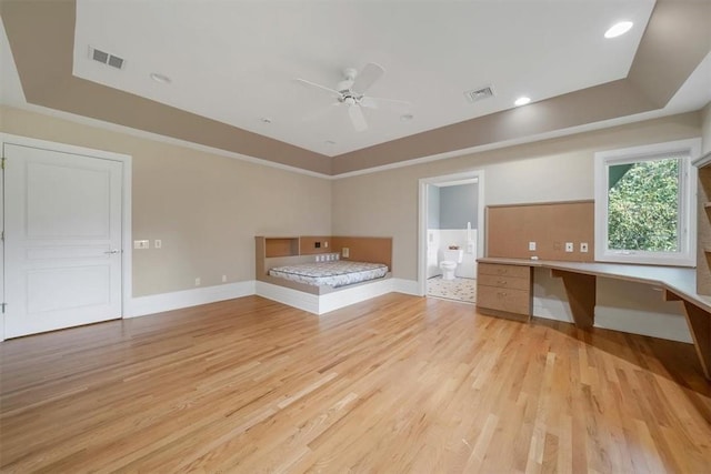 unfurnished bedroom featuring ensuite bathroom, light hardwood / wood-style floors, a raised ceiling, and built in desk