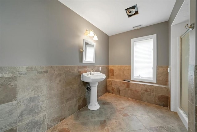 bathroom with vaulted ceiling, a healthy amount of sunlight, and tile walls