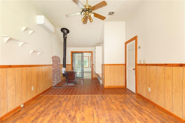 empty room with a wall mounted air conditioner, dark hardwood / wood-style floors, ceiling fan, and a wood stove