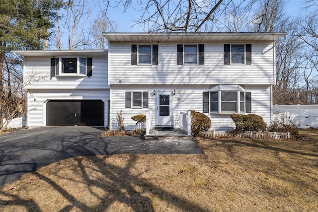 colonial home featuring driveway, a front lawn, an attached garage, and fence