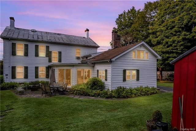 back house at dusk featuring a yard and a patio