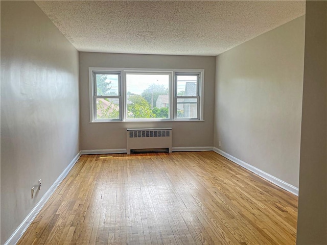 spare room featuring radiator heating unit, light hardwood / wood-style floors, and a textured ceiling