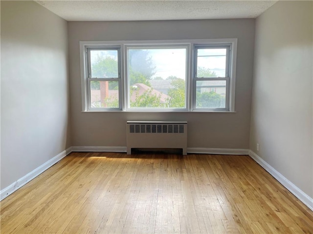 spare room with radiator heating unit, light hardwood / wood-style floors, and a textured ceiling