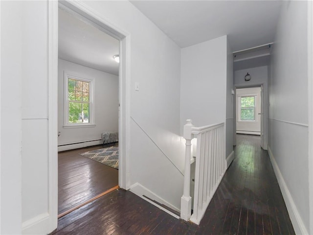 corridor featuring dark hardwood / wood-style floors, baseboard heating, and a wealth of natural light