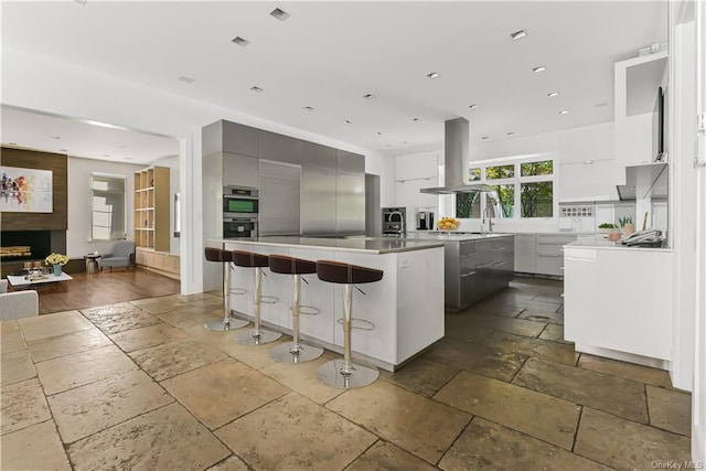 kitchen with gray cabinetry, a breakfast bar, island range hood, a spacious island, and sink