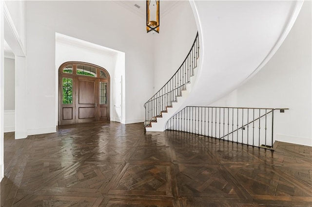 foyer entrance with dark parquet flooring, a towering ceiling, and ornamental molding