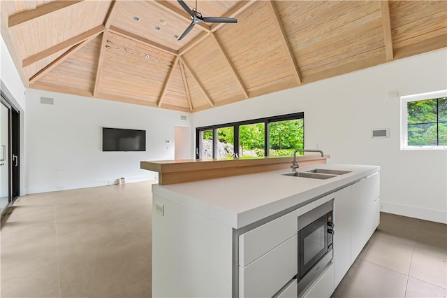 kitchen featuring black microwave, sink, beam ceiling, wooden ceiling, and white cabinetry