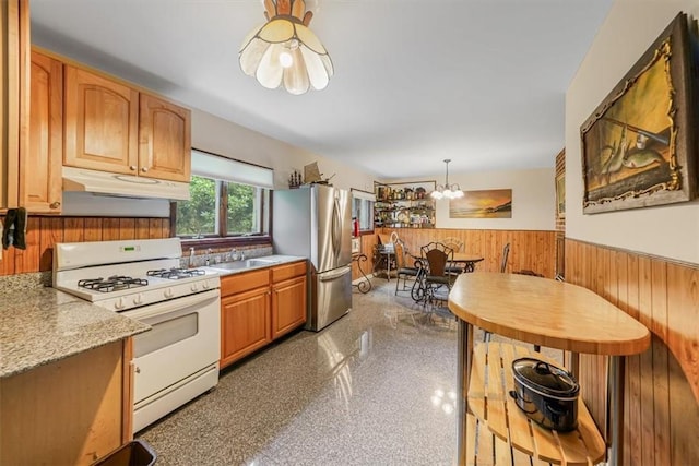 kitchen featuring white range with gas cooktop, decorative light fixtures, an inviting chandelier, stainless steel refrigerator, and wood walls