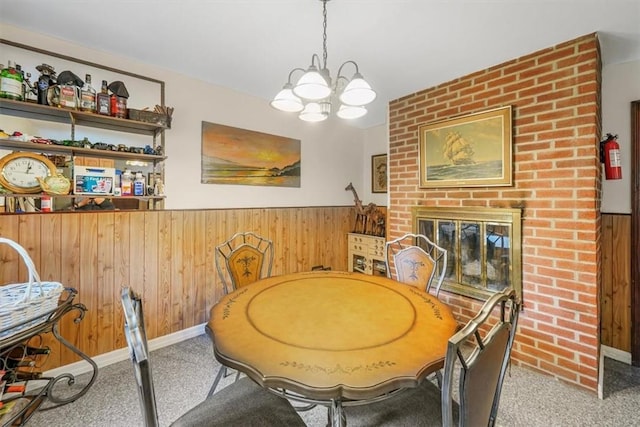 dining area with a brick fireplace, wood walls, light colored carpet, and an inviting chandelier