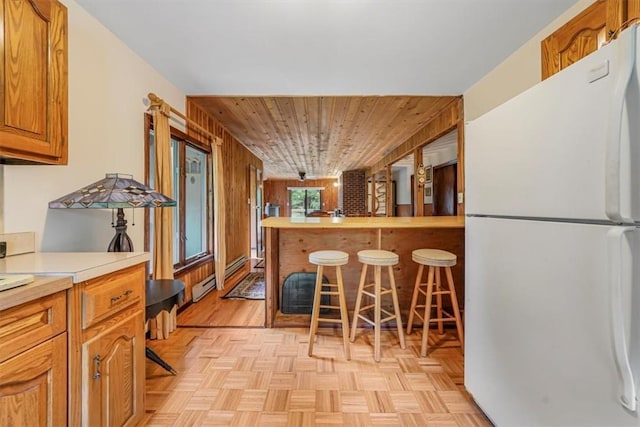 kitchen with a breakfast bar, wooden ceiling, wooden walls, white fridge, and light parquet flooring