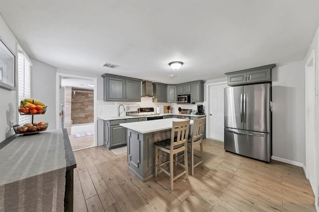 kitchen with light wood-type flooring, gray cabinetry, a breakfast bar, stainless steel appliances, and a center island