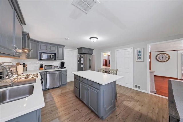 kitchen with sink, light hardwood / wood-style floors, gray cabinets, a kitchen island, and appliances with stainless steel finishes