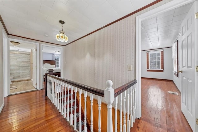 corridor with hardwood / wood-style flooring, ornamental molding, and an inviting chandelier