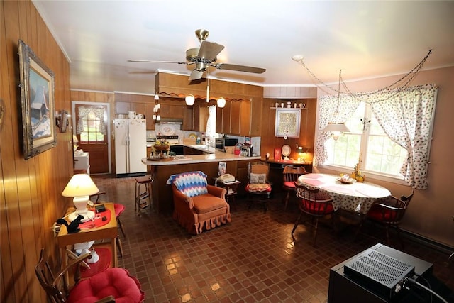 kitchen with kitchen peninsula, white refrigerator, a healthy amount of sunlight, and wood walls