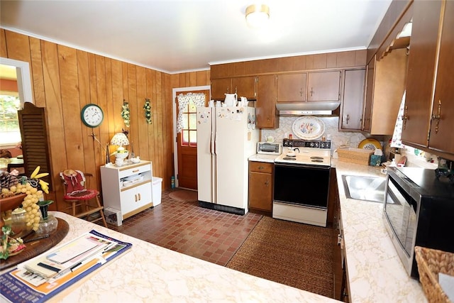 kitchen with white appliances, crown molding, sink, wooden walls, and decorative backsplash