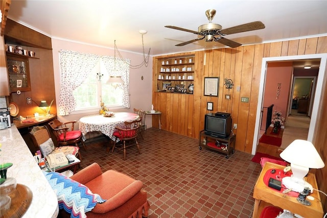 living room with wood walls, crown molding, and ceiling fan