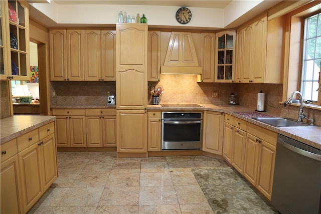 kitchen with appliances with stainless steel finishes, premium range hood, light brown cabinetry, and sink