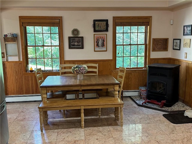 dining area with wooden walls, a wood stove, baseboard heating, and a wealth of natural light