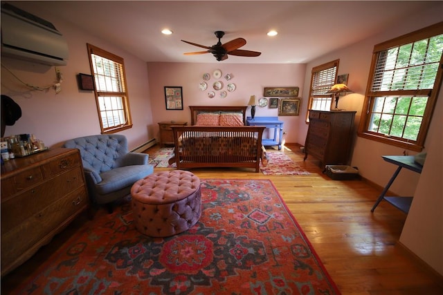 bedroom with light hardwood / wood-style flooring, baseboard heating, and a wall unit AC