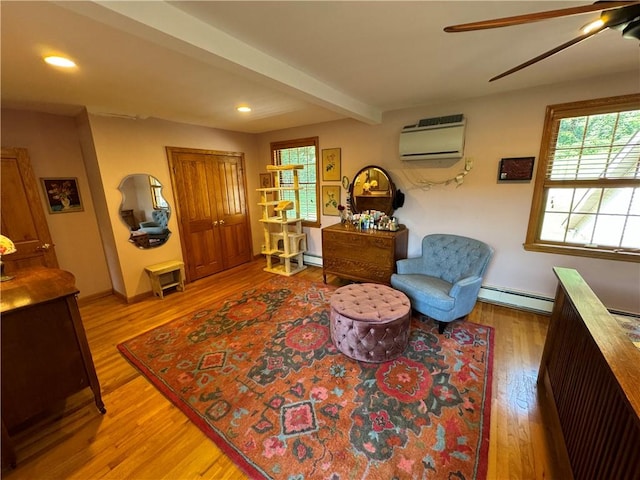 sitting room featuring light wood-type flooring, ceiling fan, a baseboard heating unit, an AC wall unit, and beamed ceiling