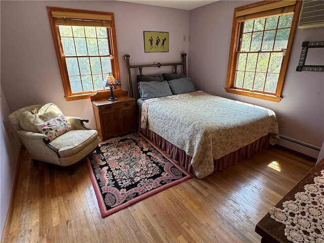 bedroom featuring a wall mounted air conditioner, wood-type flooring, a baseboard radiator, and multiple windows