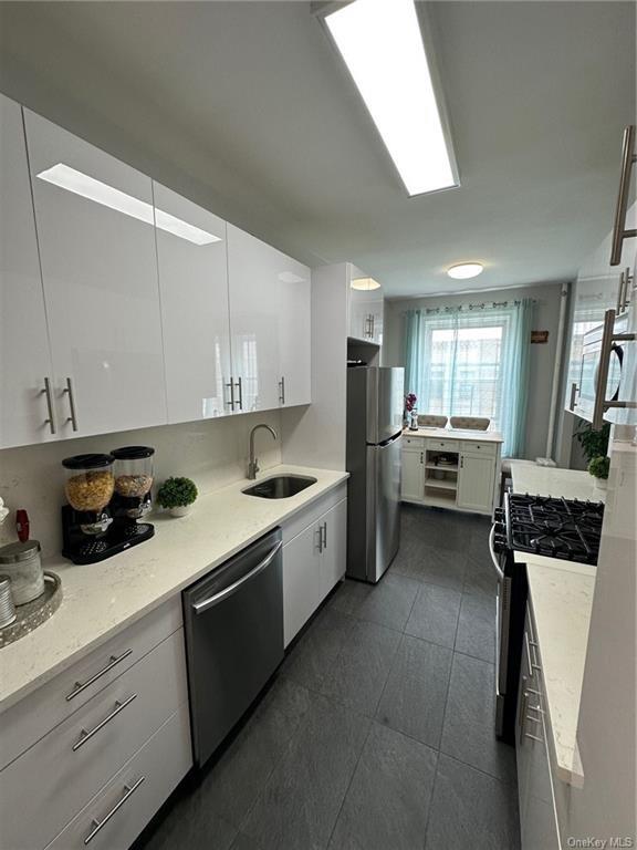 kitchen featuring light stone countertops, sink, white cabinets, dark tile patterned flooring, and appliances with stainless steel finishes