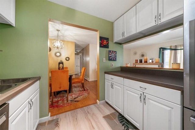 kitchen with sink, light hardwood / wood-style flooring, stainless steel dishwasher, a chandelier, and white cabinets