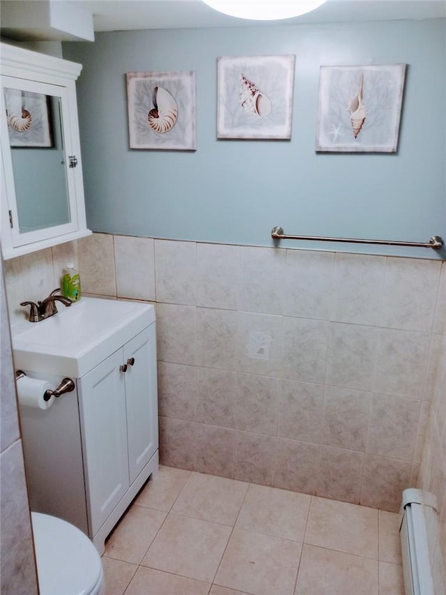 bathroom featuring baseboard heating, tile patterned floors, toilet, vanity, and tile walls