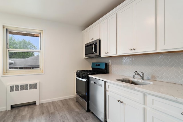 kitchen with appliances with stainless steel finishes, sink, light hardwood / wood-style flooring, radiator heating unit, and white cabinetry