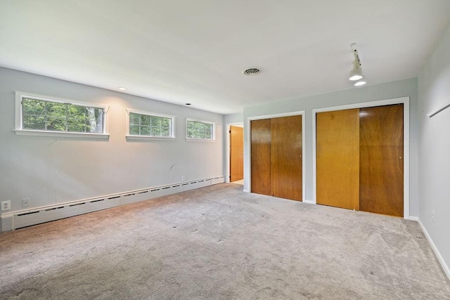 unfurnished bedroom featuring carpet, a baseboard radiator, multiple windows, and multiple closets