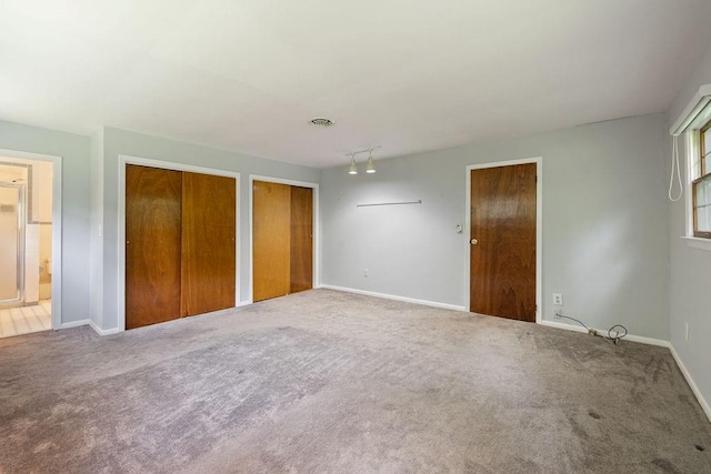 unfurnished bedroom featuring carpet flooring, connected bathroom, and multiple closets