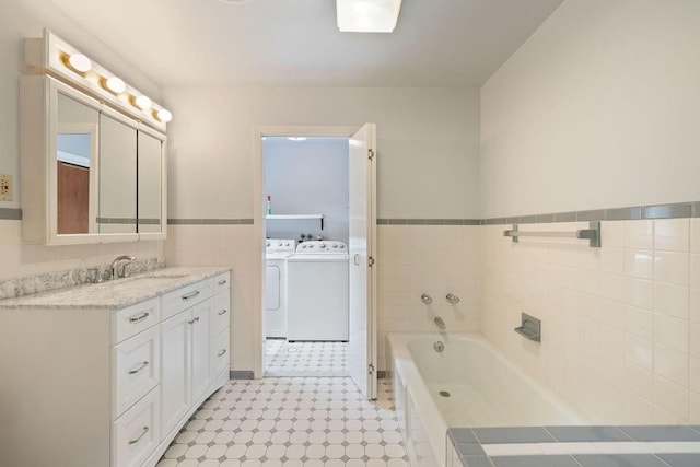 bathroom featuring washing machine and clothes dryer, a tub to relax in, vanity, and tile walls