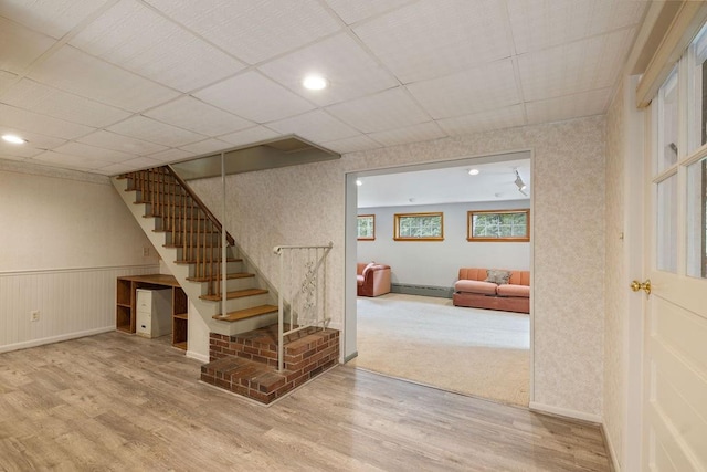 basement with a paneled ceiling, wood-type flooring, and a baseboard radiator